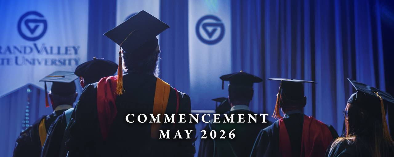 Faculty wearing regalia stand during GVSU Commencement ceremony